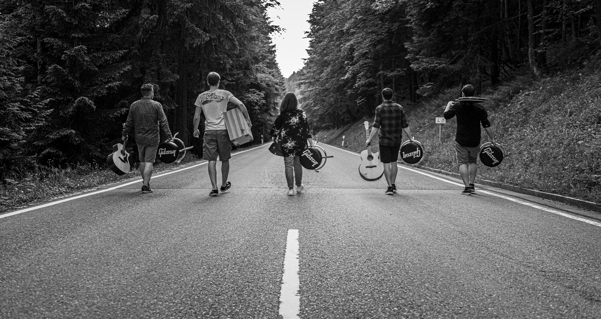 Gruppenfoto von BAM. Die Bandmitglieder gehen mit ihren Instrumente eine Strasse hinab