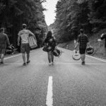 Gruppenfoto von BAM. Die Bandmitglieder gehen mit ihren Instrumente eine Strasse hinab