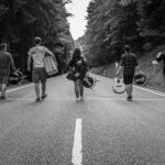 Gruppenfoto von BAM. Die Bandmitglieder gehen mit ihren Instrumente eine Strasse hinab