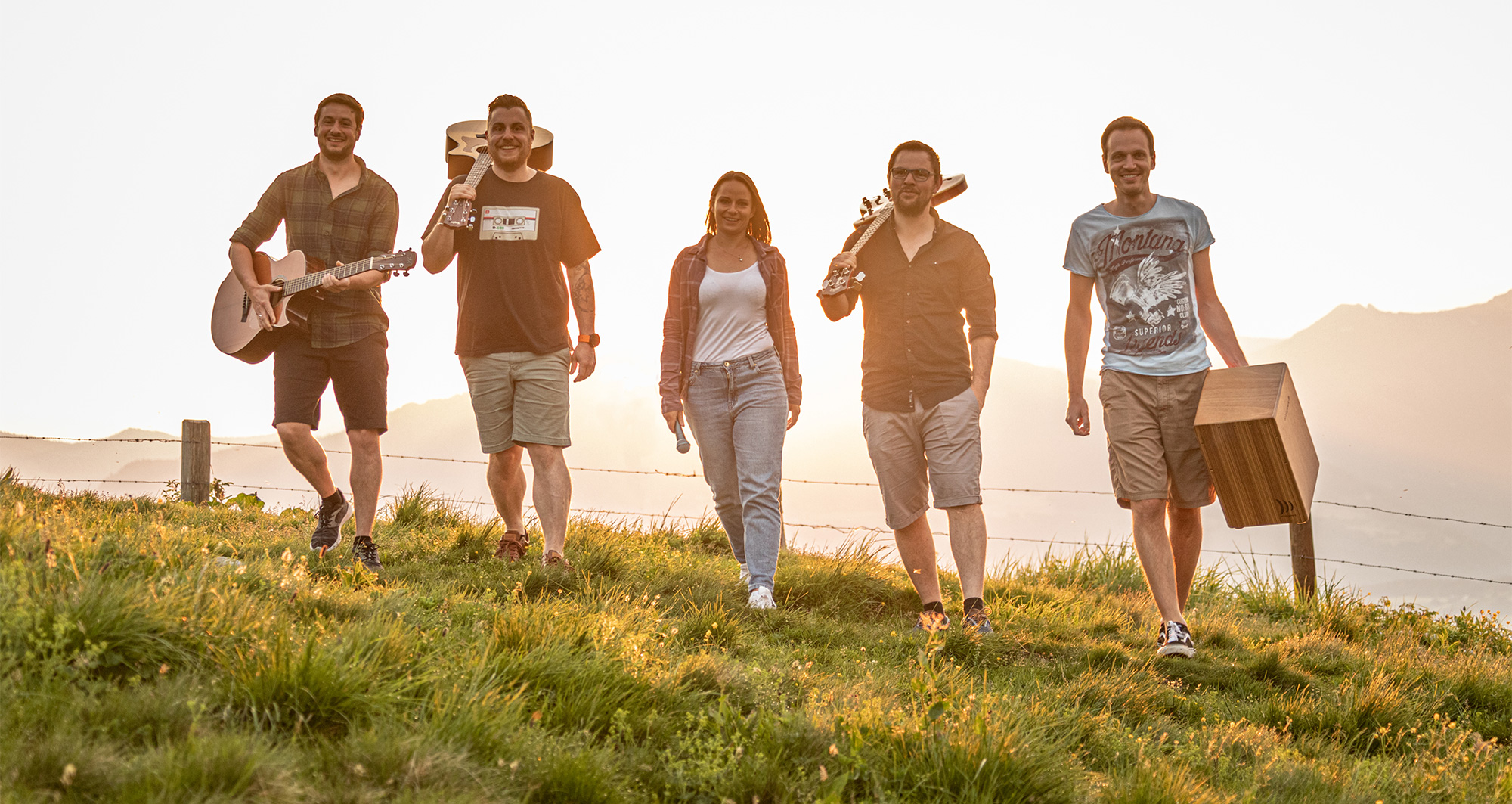 Gruppenfoto von BAM Berchtesgaden Akustik Musik. Mit den Instrumenten über die Schulter gehen die 5 Musikanten über eine Alpenwiese.